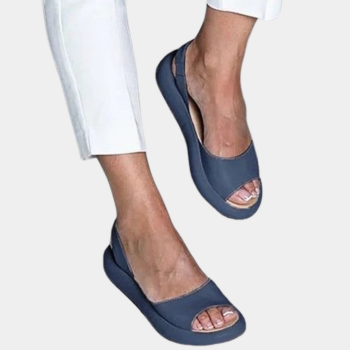 Blauwe dames sandalen met open teen en elastische band, gedragen met witte broek. Comfortabele zomerschoenen, ideaal voor casual en formele gelegenheden.