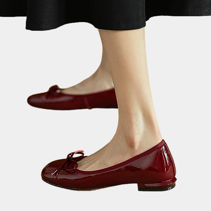 Rode lakleren ballerina's met strikdetail, gedragen door vrouw in zwarte rok. Stijlvolle damesmode, comfortabele platte schoenen.