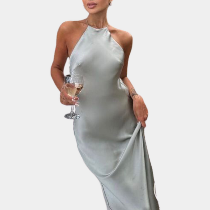 Grijze satijnen halterjurk met open rug, gedragen door vrouw met wijnglas. Elegante avondjurk, perfect voor feestelijke gelegenheden.