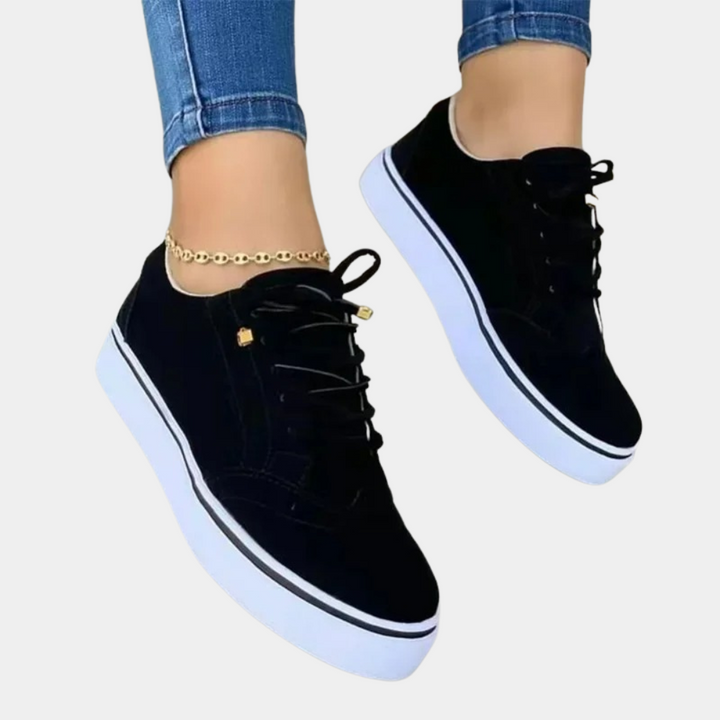 Zwarte sneakers met witte zolen, gedragen door persoon met blauwe jeans en gouden enkelbandje. Stijlvolle casual schoenen voor dagelijks gebruik.