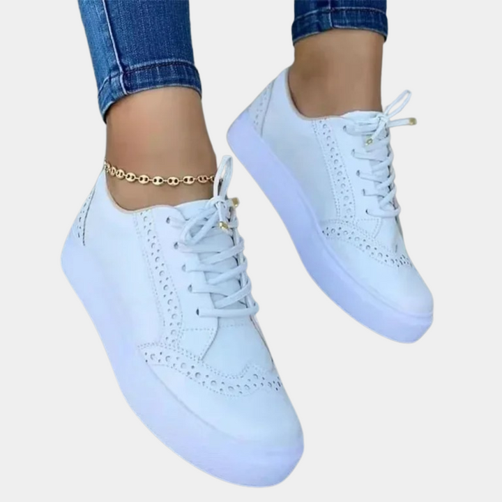 Witte leren sneakers met perforatiedetails, gedragen met blauwe jeans en gouden enkelbandje. Modieuze dames schoenen, casual stijl.