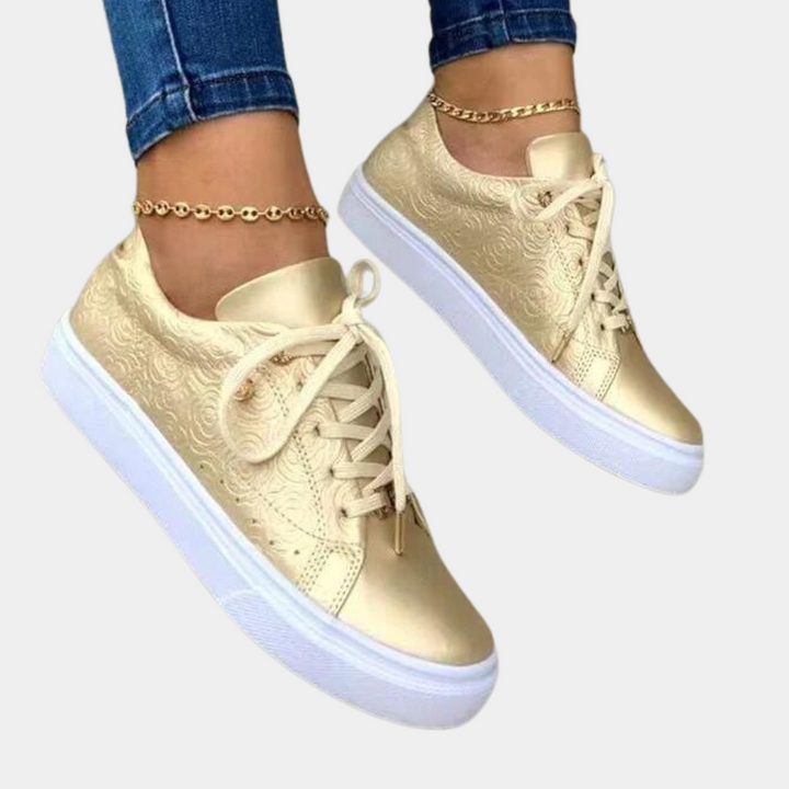 Gouden damessneakers met witte zool, sierlijk patroon en veters, gedragen met enkelbandje. Trendy schoenen, casual stijl, comfortabele pasvorm.