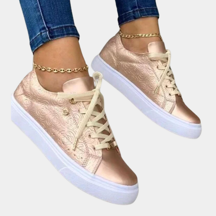 Roze gouden damessneakers met witte zolen en bloemendessin, gedragen met enkelbandjes. Trendy casual schoenen voor dames.