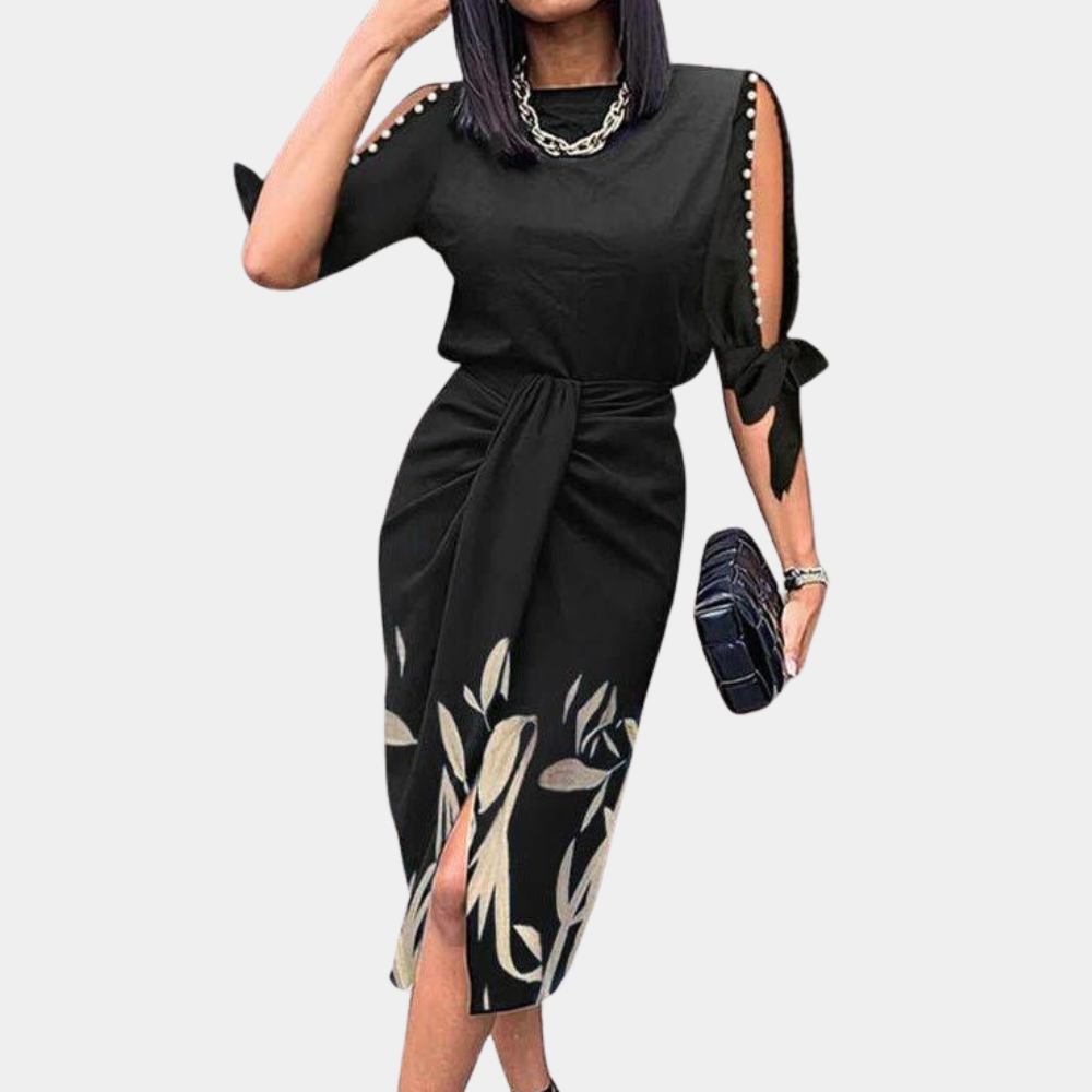 Zwarte midi-jurk met bloemenprint, open schouders en knoopdetails. Perfect voor elegante damesmode. Accessoires: zilveren ketting, zwarte clutch.