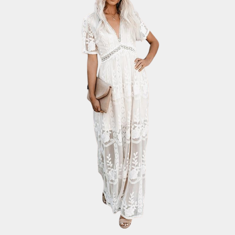 Witte kanten maxi-jurk met korte mouwen en V-hals, gedragen door een vrouw met een beige clutch. Perfect voor zomerse bruiloften en strandfeesten.