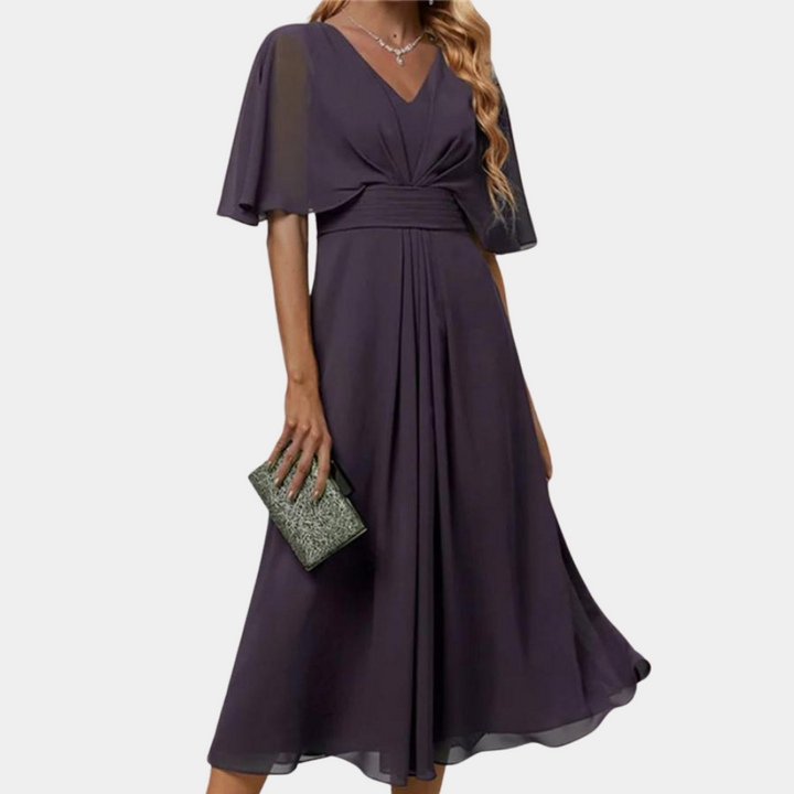 Paarse avondjurk met V-hals en korte mouwen, gedragen door model met glitter clutch. Elegante damesmode, perfect voor speciale gelegenheden.
