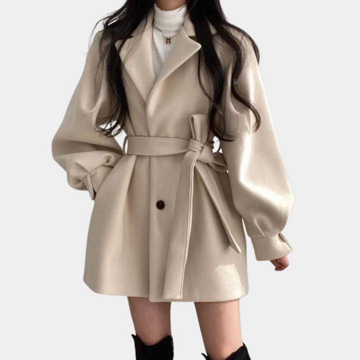 Damesjas in abrikooskleur met ceintuur, lange pofmouwen en knoopsluiting. Stijlvolle herfst- en wintermode. Elegante en trendy jas.