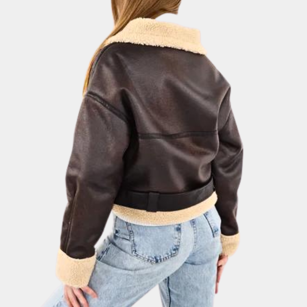 Vrouw in bruine leren jas met schapenvachtkraag en manchetten, gecombineerd met blauwe jeans. Modieuze winterkleding, trendy damesmode.