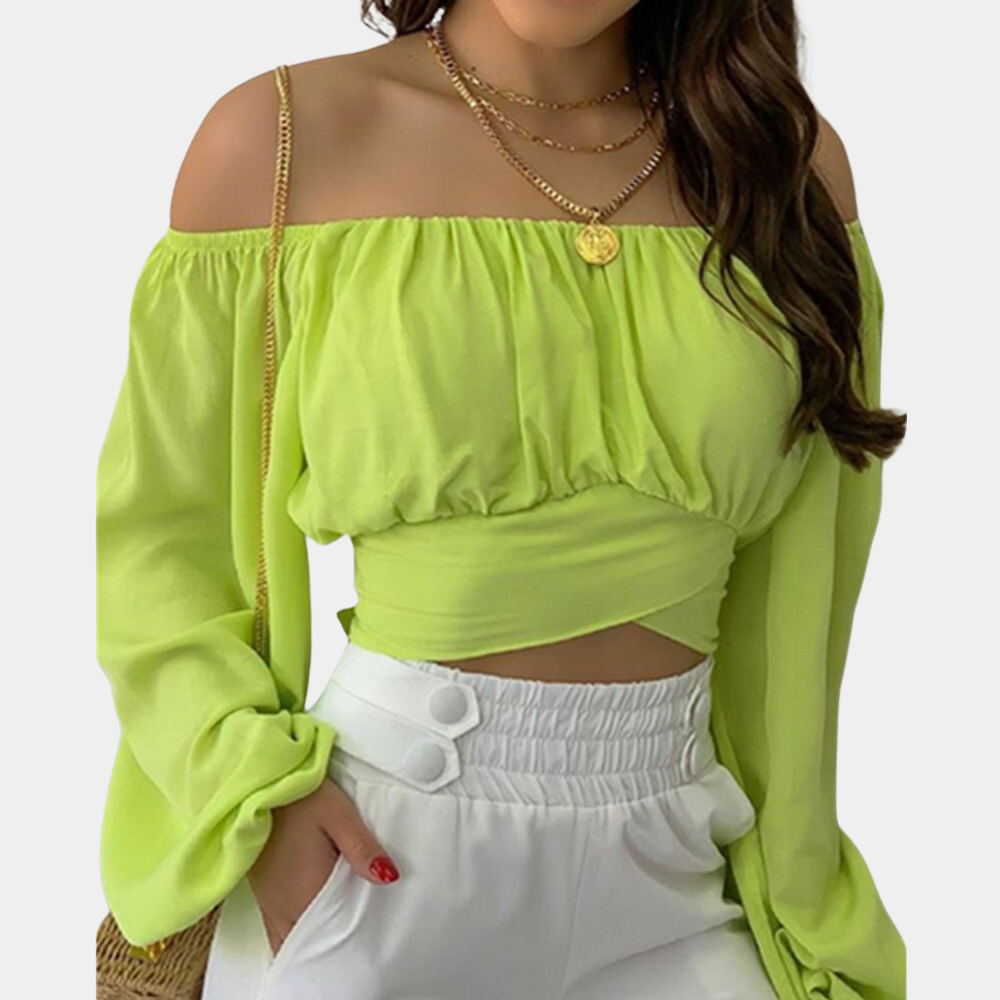 Vrouw in limegroene off-shoulder blouse met lange mouwen en gouden kettingen, gecombineerd met witte broek. Trendy damesmode, zomeroutfit.