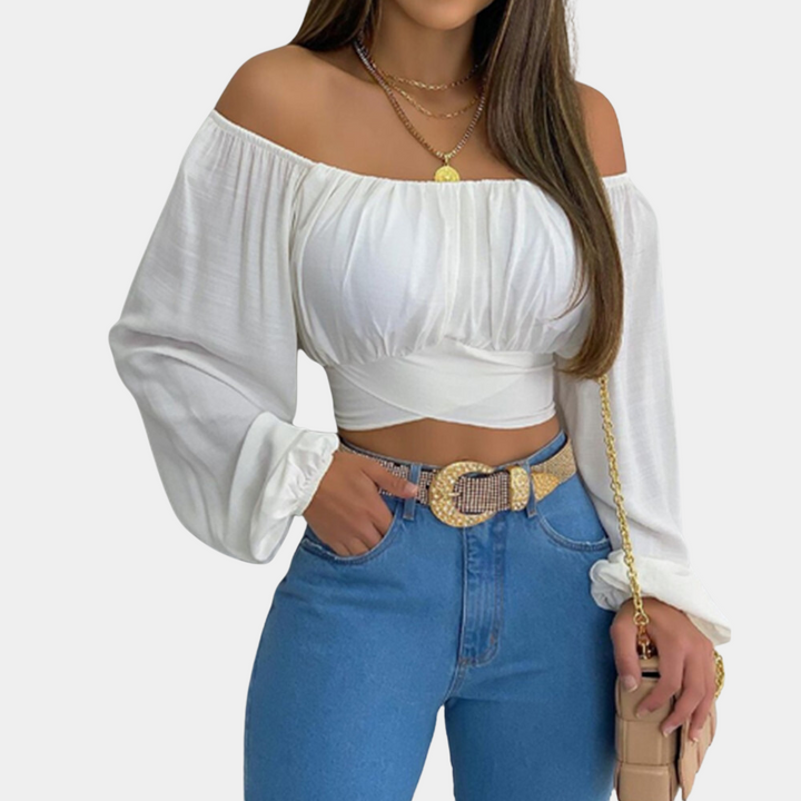 Vrouw in witte off-shoulder blouse met lange mouwen, blauwe jeans en gouden ketting. Trendy damesmode, casual chique outfit.