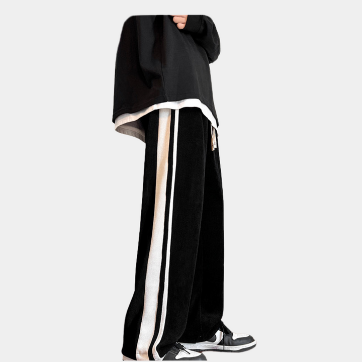 Zwarte wijde broek met witte zijstrepen, gedragen met zwarte trui en sneakers. Modieuze streetwear outfit voor casual stijl.