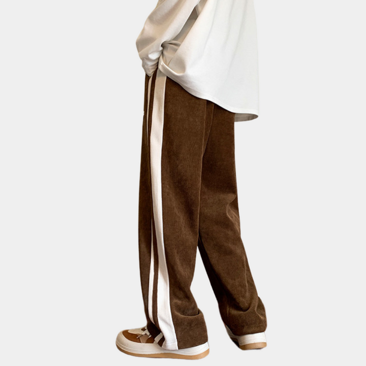 Bruine corduroy broek met witte zijstrepen, gedragen door persoon in witte trui en bruine sneakers. Modieuze casual kleding voor heren.