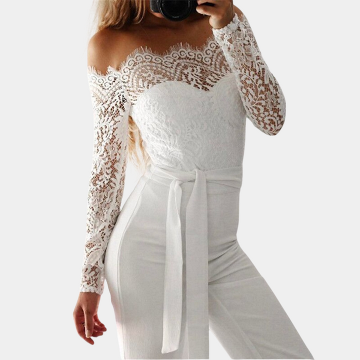 Vrouw in elegante witte kanten jumpsuit met lange mouwen en strikceintuur, modieuze dameskleding, stijlvolle outfit voor speciale gelegenheden.