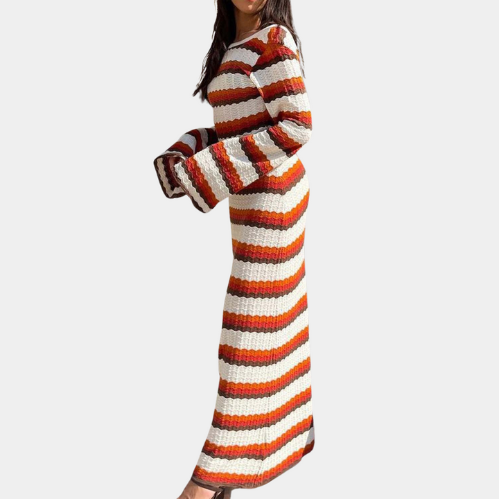 Vrouw in lange, gebreide jurk met rood-wit-oranje strepen, wijde mouwen. Modetrend herfst 2023, comfortabele dameskleding.
