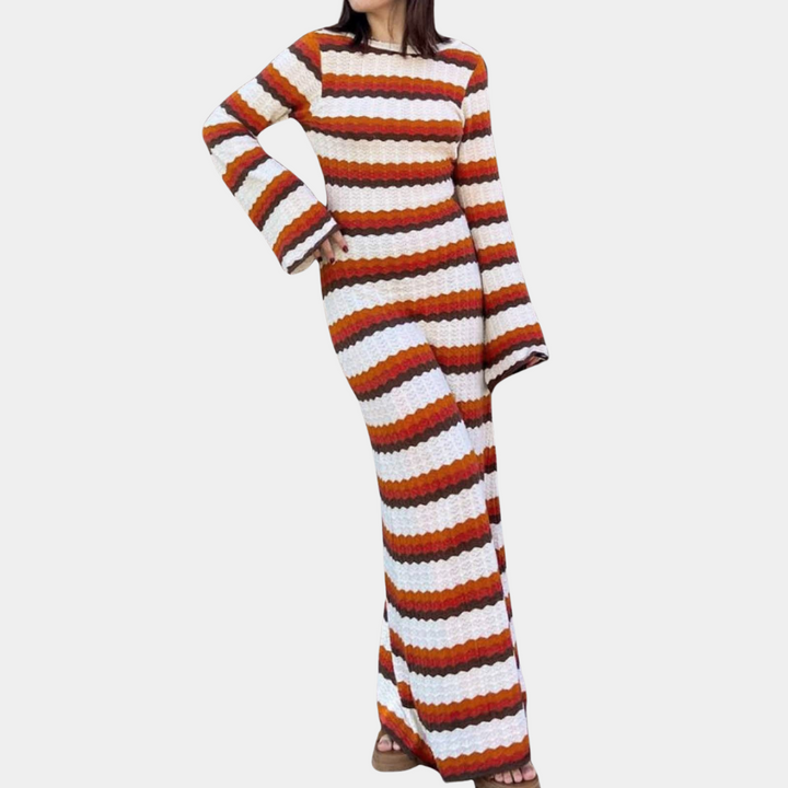 Vrouw in lange, gebreide jurk met oranje, bruine en witte strepen, wijde mouwen. Modieuze herfstkleding, boho-stijl, comfortabele pasvorm.