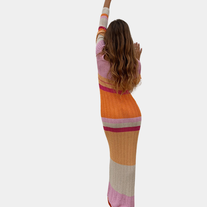 Vrouw in kleurrijke, gestreepte maxi-jurk met lange mouwen, roze en oranje tinten, modetrend, herfstkleding, stijlvolle damesmode.