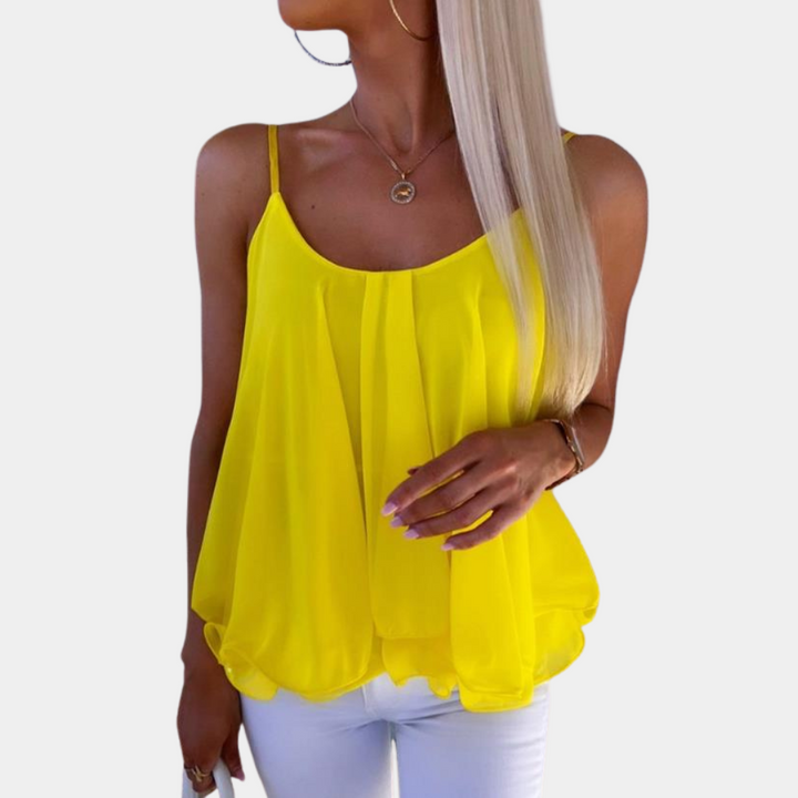 Vrouw in gele chiffon top met spaghettibandjes, gecombineerd met witte broek. Trendy zomermode, casual dameskleding, stijlvolle outfit.