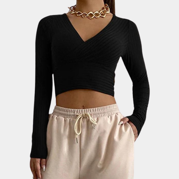 Zwarte dames crop top met lange mouwen en V-hals, gecombineerd met beige joggingbroek. Modieuze outfit, ideaal voor casual en trendy looks.