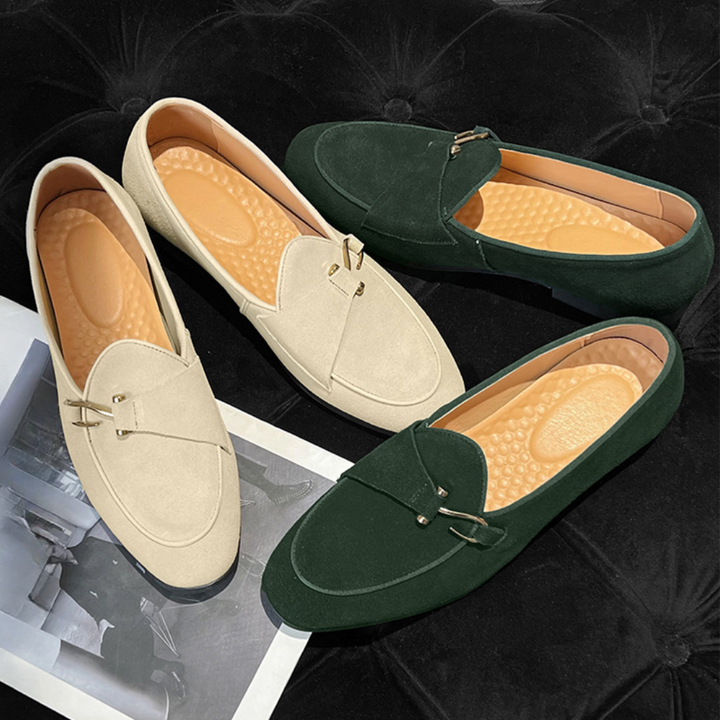 Twee paar loafers, één beige en één groen, met metalen details en comfortabele binnenzolen, op een zwarte achtergrond met tijdschrift.
