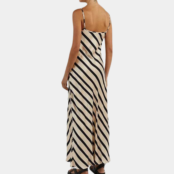 Vrouw in lange, mouwloze jurk met zwart-witte diagonale strepen, elegante zomerjurk, modetrend, casual stijl, achterkant zichtbaar.