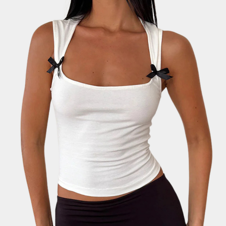 Vrouw draagt witte tanktop met zwarte strikjes, mouwloos ontwerp, modieuze dameskleding, casual stijl, perfect voor zomeroutfits.