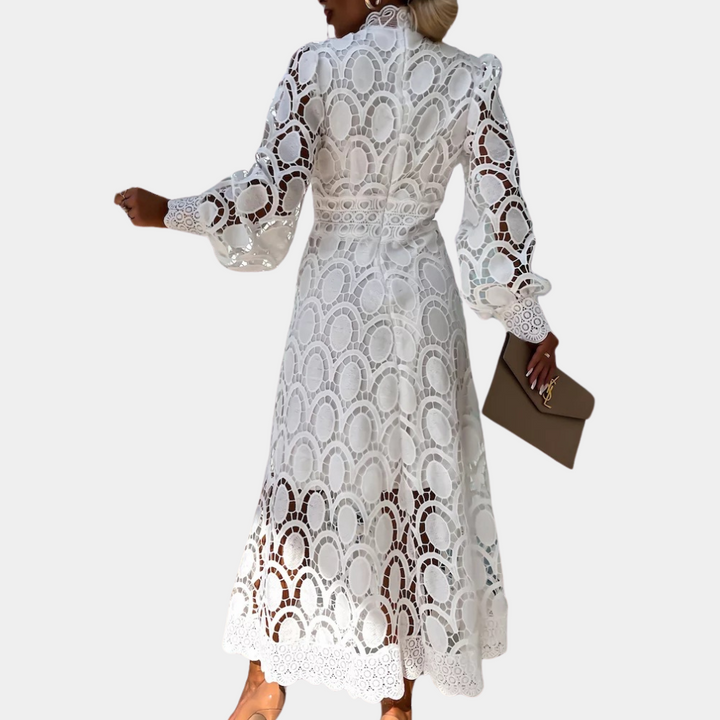 Witte kanten jurk met lange mouwen en elegant patroon, gedragen door vrouw met clutch. Perfect voor zomerse evenementen en bruiloften.
