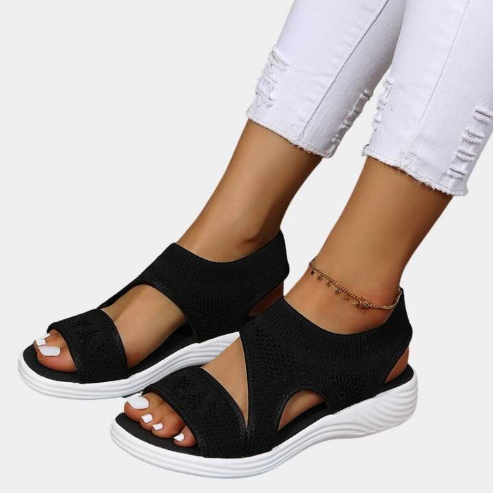 Zwarte dames sandalen met open teen en witte zool, gedragen met witte gescheurde jeans. Comfortabele zomerschoenen, modieus en casual.