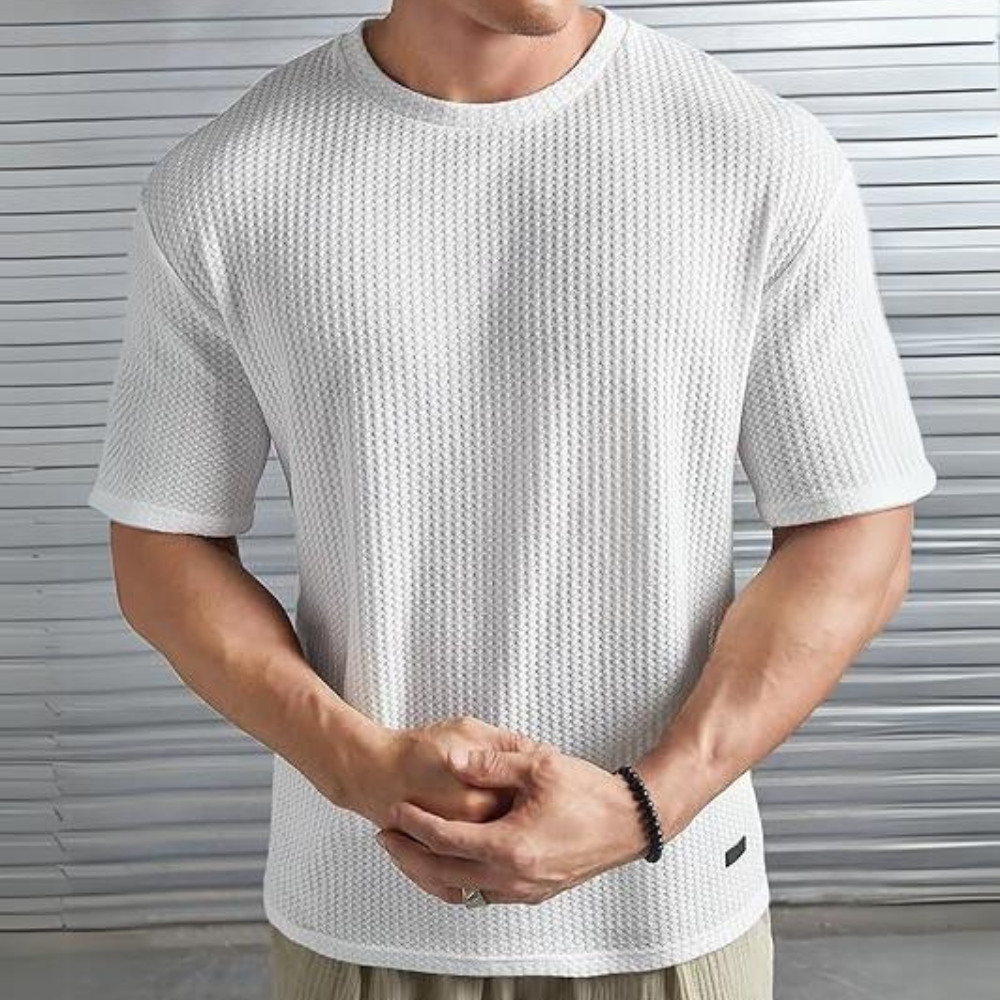 Man in witte, gebreide T-shirt met korte mouwen, voor metalen achtergrond. Stijlvolle herenkleding, casual mode, comfortabele textuur.
