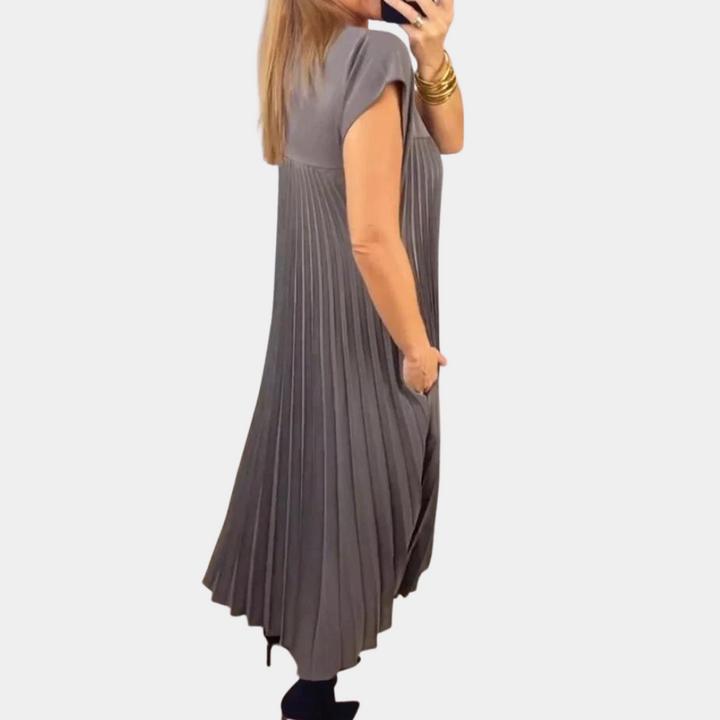Grijze geplooide jurk met korte mouwen, gedragen door vrouw. Elegante damesmode, comfortabele pasvorm, geschikt voor casual en formele gelegenheden.