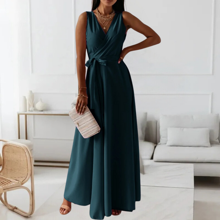 Donkergroene maxi-jurk met V-hals en strikceintuur, gedragen door model in moderne woonkamer. Perfect voor elegante avondkleding.