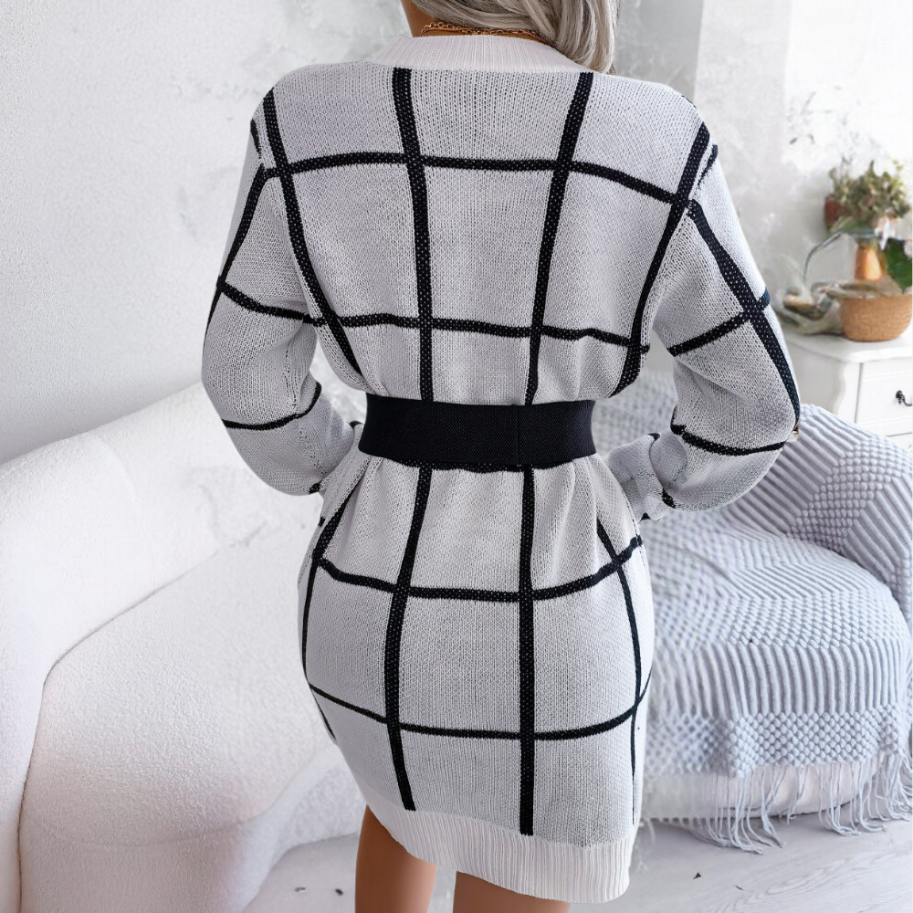 Vrouw draagt gebreide jurk met zwart-wit ruitpatroon, lange mouwen en ceintuur. Stijlvolle wintermode, perfect voor casual en chique gelegenheden.
