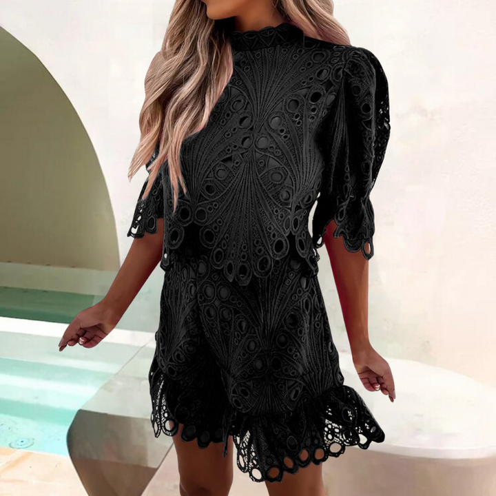 Zwarte kanten jurk met korte mouwen en golvende zoom, gedragen door vrouw met lang blond haar. Perfect voor zomerfeestjes en elegante gelegenheden.