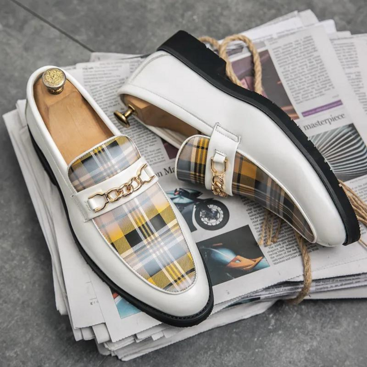 Witte leren loafers met geel geruit patroon en gouden kettingdetail, stijlvolle herenschoenen op stapel kranten, luxe modeaccessoire.