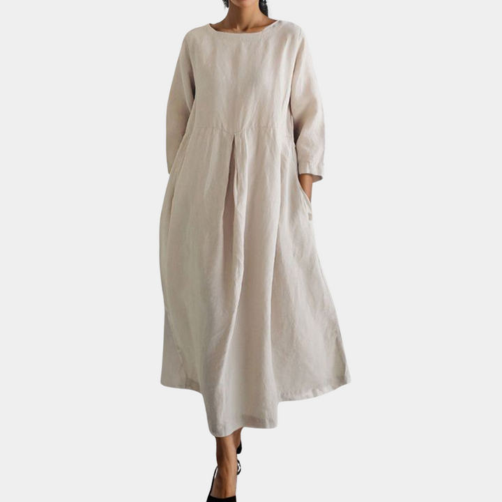 Vrouw in lange, losse, abrikooskleurige linnen jurk met driekwart mouwen en zakken. Ideaal voor casual lente- en zomeroutfits.