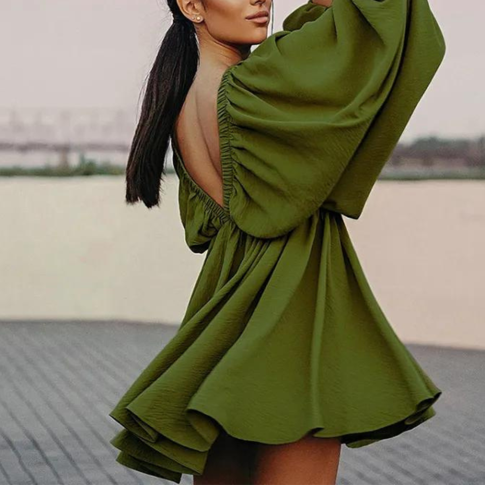 Vrouw in groene jurk met open rug en wijde mouwen, draaiend op een buitenlocatie. Trendy damesmode, elegante avondjurk, stijlvolle kleding.