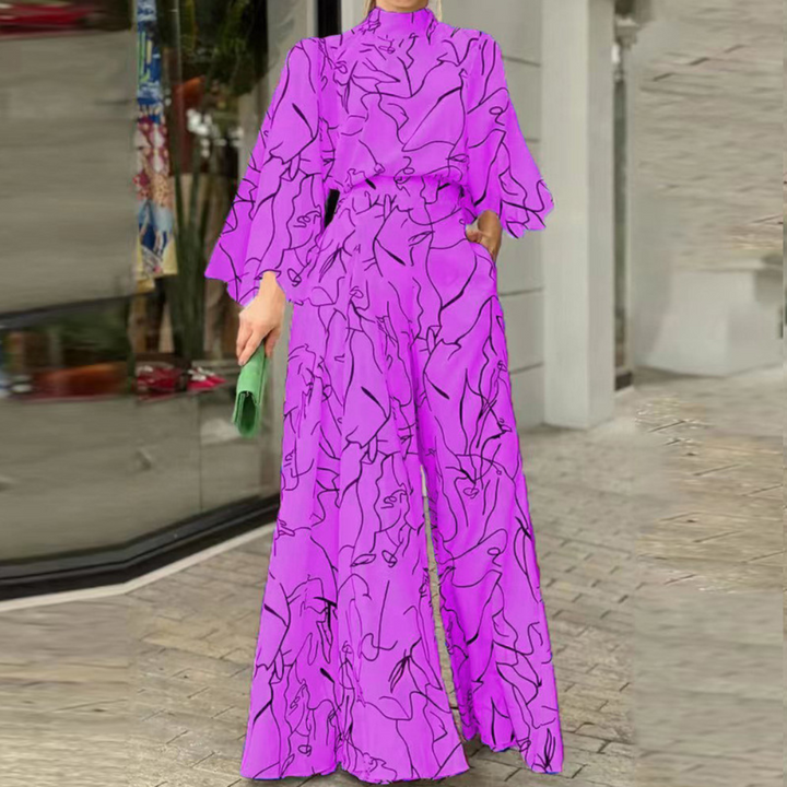 Paarse jumpsuit met abstracte zwarte lijnen, wijde pijpen en lange mouwen, gedragen door een model. Trendy damesmode, opvallende outfit.