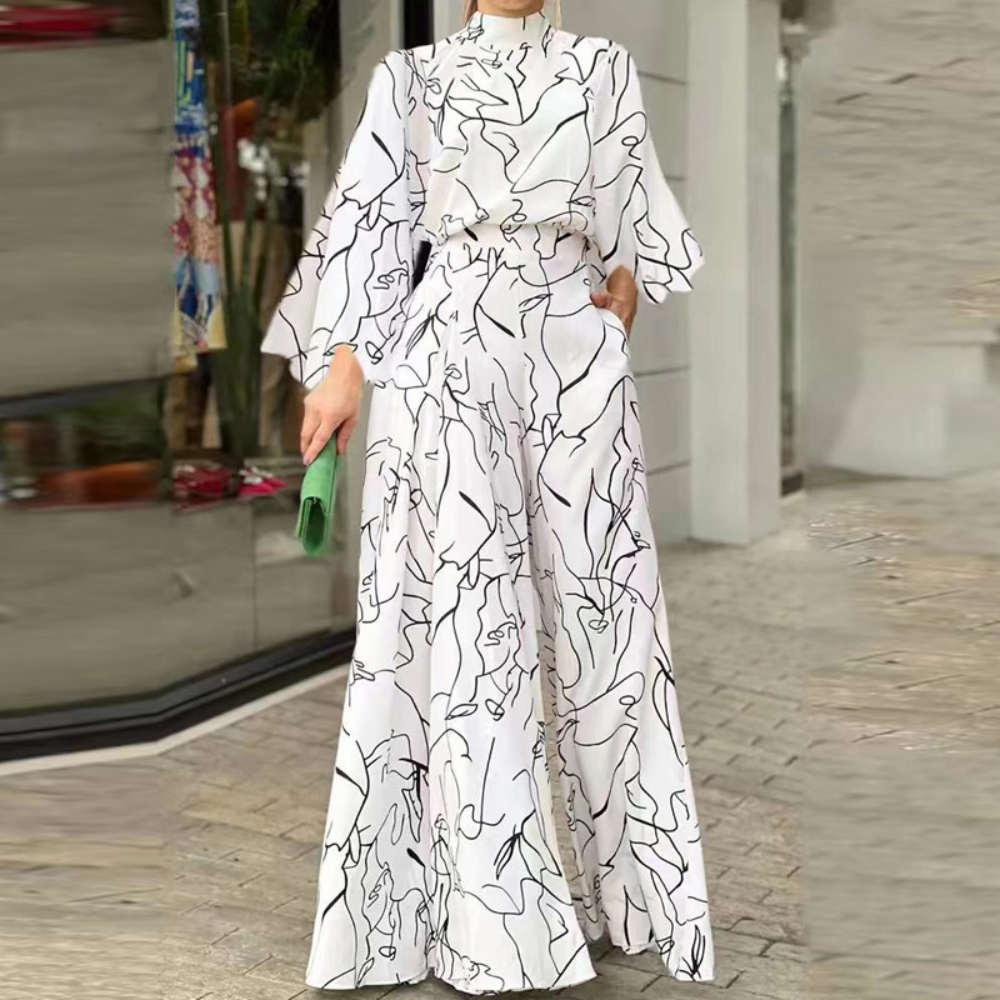 Vrouw in witte jumpsuit met abstracte zwarte lijnen, wijde pijpen en lange mouwen, poseert buiten bij glazen etalage. Modieuze dameskleding.