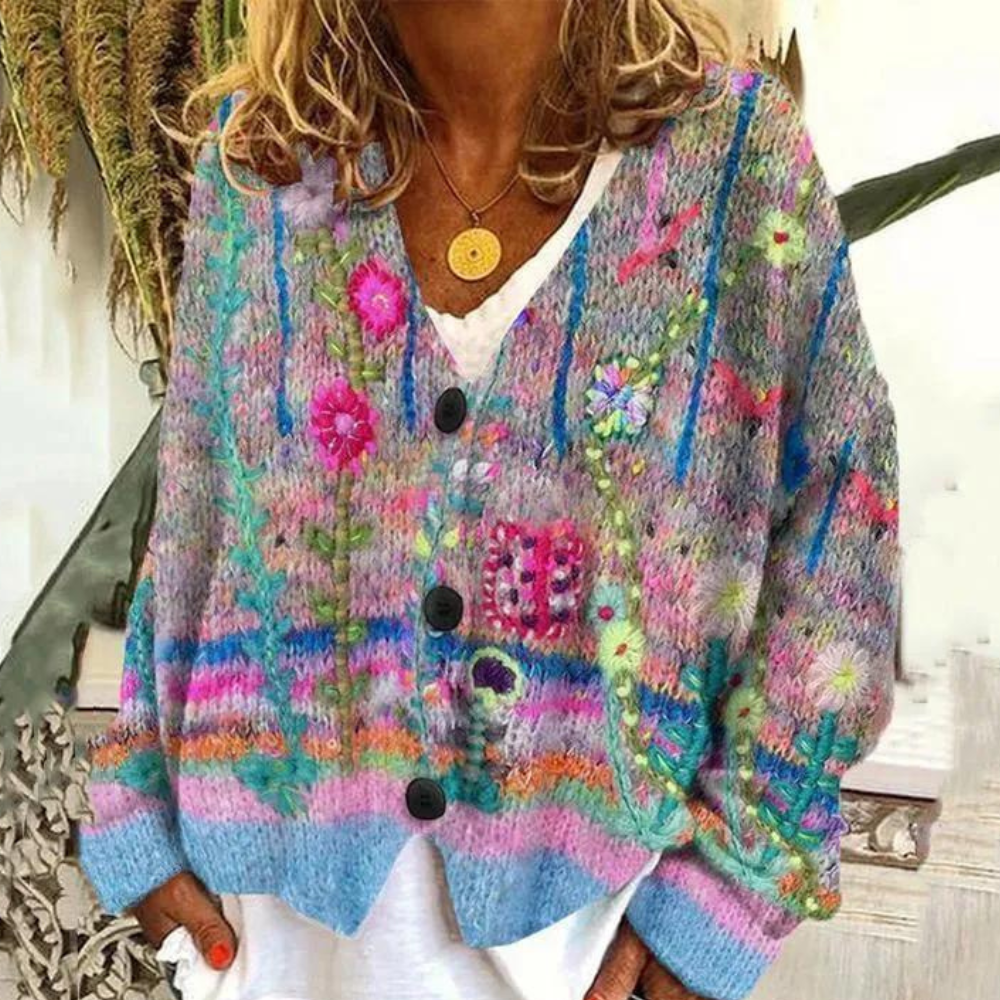 Vrouw draagt kleurrijk gebreid vest met bloemenpatroon, blauwe en roze tinten. Perfect voor boho-mode, herfstkleding, casual stijl.