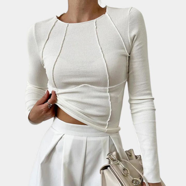 Witte damestrui met lange mouwen en siernaden, gecombineerd met een witte geplooide rok en een beige handtas. Perfect voor een stijlvolle look.