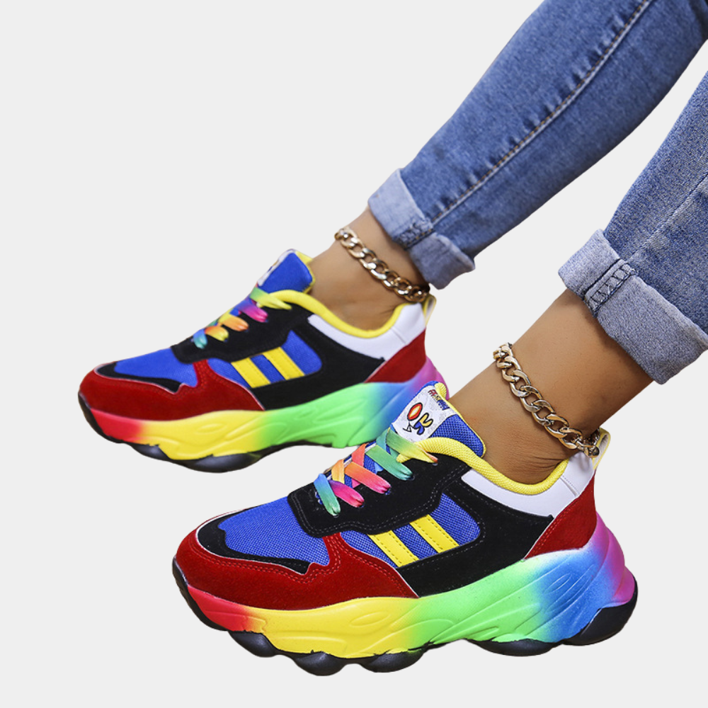 Vrouw draagt kleurrijke sneakers met regenboogzool en blauwe jeans. Trendy mode, opvallende sportschoenen, casual stijl, streetwear.