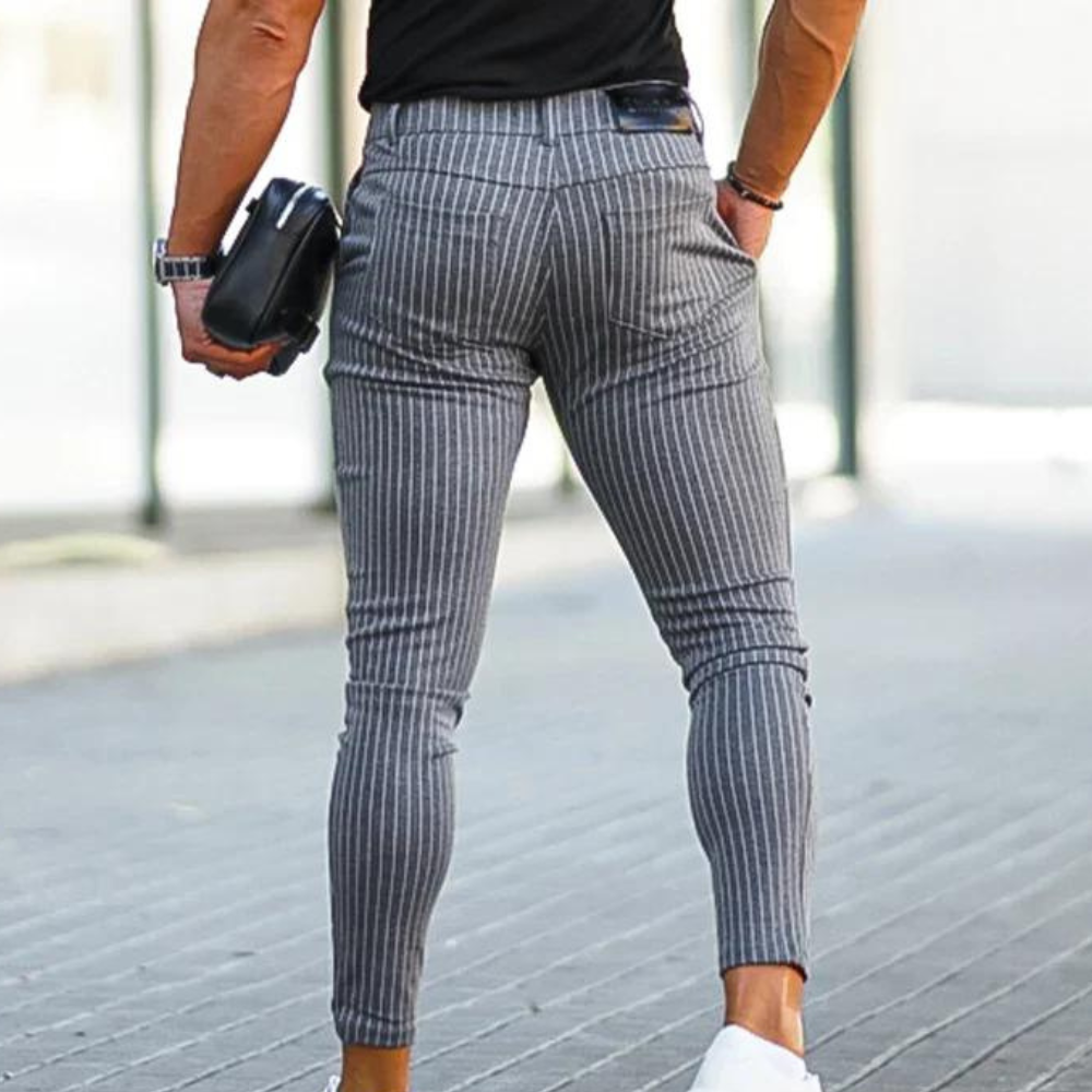 Grijze gestreepte herenbroek, slim fit, gedragen door een man met zwarte top en witte sneakers. Modieuze casual stijl, straatmode.
