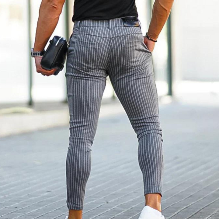 Grijze gestreepte herenbroek, slim fit, gedragen door een man met zwarte top en witte sneakers. Modieuze casual stijl, straatmode.