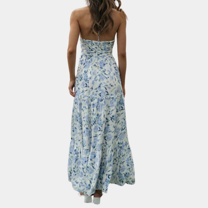 Vrouw in lange, blauwe bloemenjurk met blote rug, zomermode, elegante maxi-jurk, casual strandkleding, trendy dameskleding.