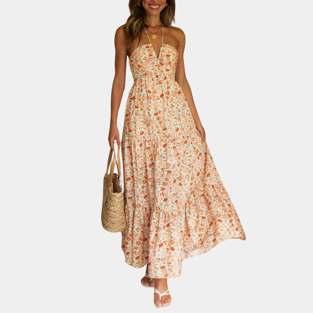 Vrouw in lange, oranje bloemenjurk met halternek en rieten tas. Zomerse damesmode, casual strandoutfit, trendy maxi-jurk.
