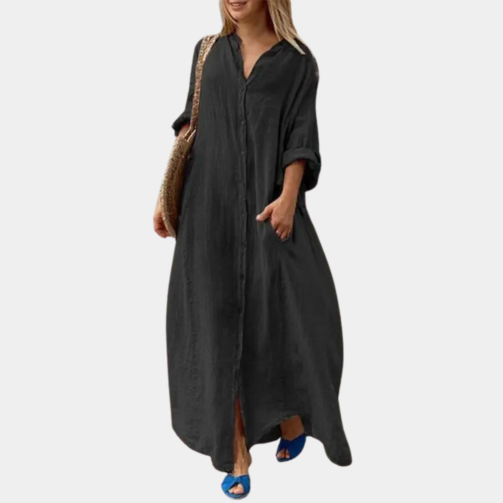 Zwarte maxi-jurk met lange mouwen, knoopsluiting en zakken, gedragen door vrouw met strooien tas en blauwe sandalen. Elegante damesmode.