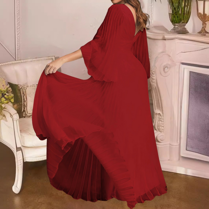Rode avondjurk met wijde mouwen en plissérok, gedragen door model in klassieke interieursetting. Elegante damesmode, stijlvolle avondkleding.