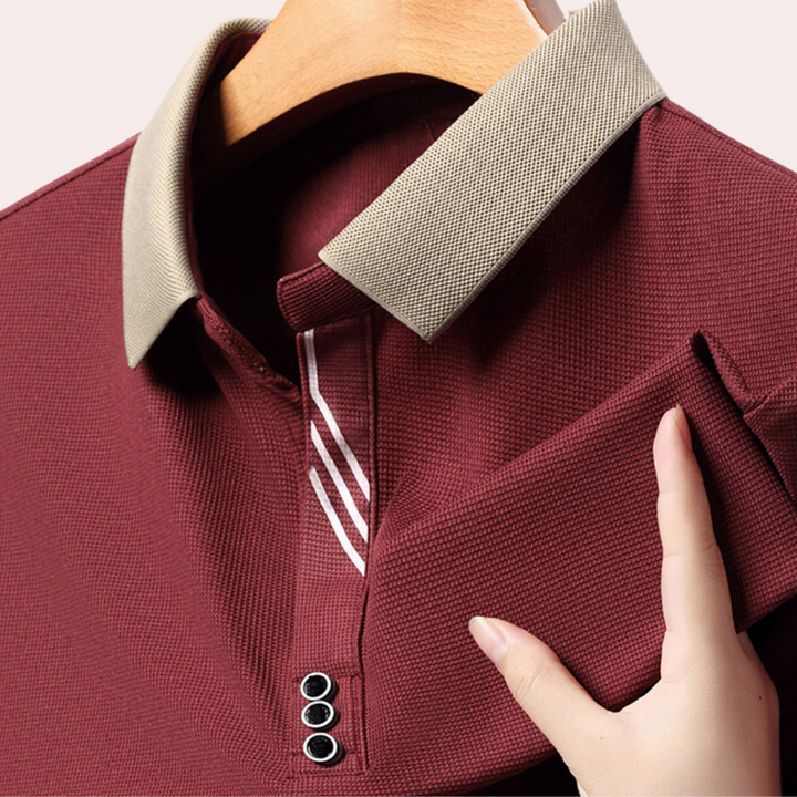 Bordeaux poloshirt met beige kraag, drieknoopsluiting en gestreepte details, op houten hanger. Hoogwaardige herenkleding, stijlvolle casual mode.