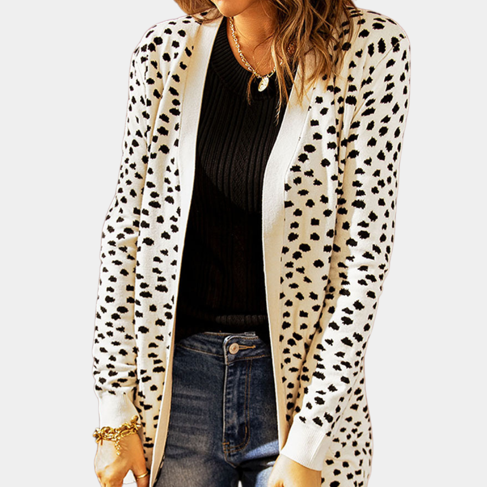 Vrouw in zwarte trui en spijkerbroek draagt een witte cardigan met zwarte stippen. Modieuze dameskleding, casual stijl, herfstoutfit.
