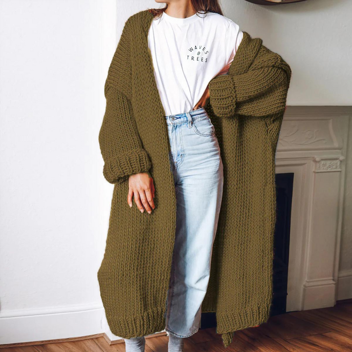Vrouw draagt lange, olijfgroene gebreide cardigan over witte T-shirt en lichte spijkerbroek. Stijlvolle herfstmode, comfortabele dameskleding.