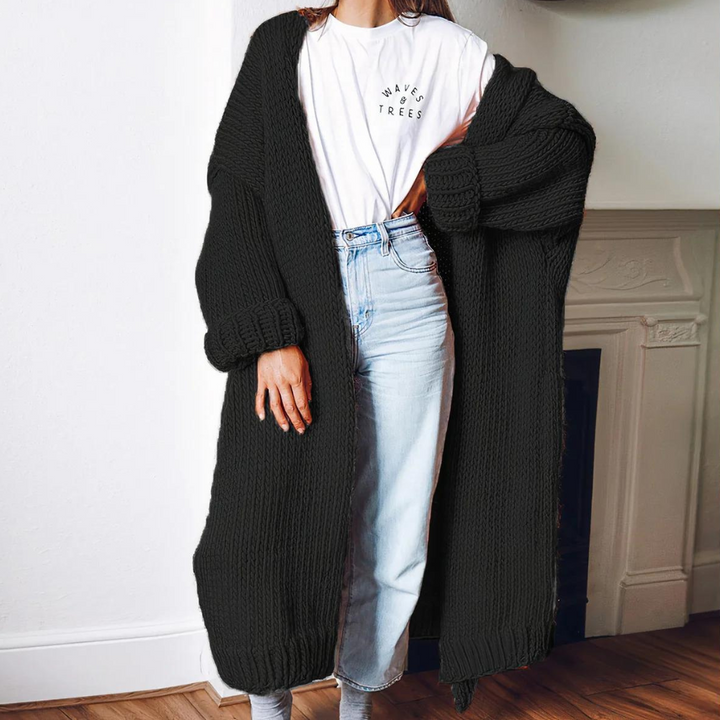 Vrouw draagt zwarte gebreide lange cardigan, witte T-shirt en lichtblauwe jeans. Stijlvolle herfstmode, comfortabele dameskleding, casual outfit.